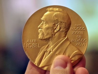 hand holding gold coin embossed with bust of Alfred Nobel