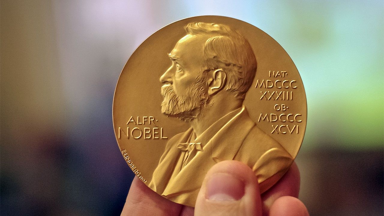 hand holding gold coin embossed with bust of Alfred Nobel