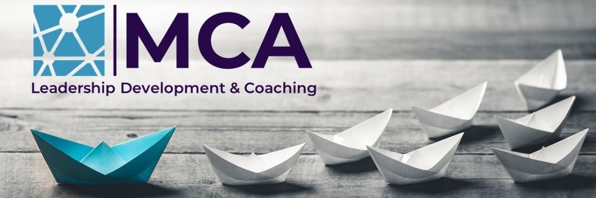 MCA logo blue paper boat at head of flotilla of 7 white paper boats on wooden boards. Leadership Development and Coaching.